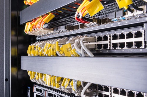 Close-up view of network switches with multiple Ethernet cables connected, suggesting a computer repair in progress. The cables have yellow tags, and the setup is inside a server rack, indicating a complex data or communication system. computer repair