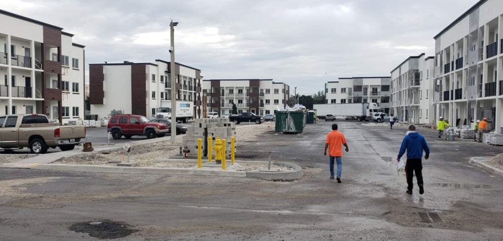 Two men walk through a construction site bustling with trucks and equipment surrounding the multi-story buildings. The overcast sky looms above as they discuss the latest computer repair techniques amidst the evolving skyline. computer repair